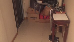 Ein Flur mit einer Tür, einem Tisch mit Stuhl und mehreren Paar Schuhen auf dem Boden.