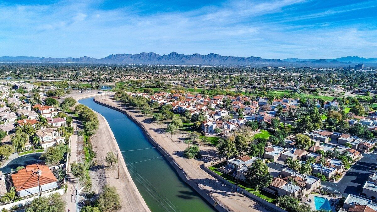 Vista aérea de una zona residencial con un río, casas y montañas al fondo.