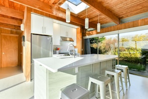 A modern kitchen with a large island, white cabinetry, stainless steel appliances, and a view of the outdoors.
