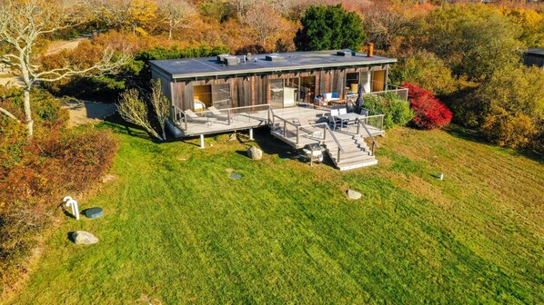 Una casa moderna con terraza y zona de estar al aire libre, rodeada de césped y árboles.