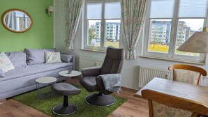 A living room with a grey sofa, two armchairs, a small round table, and a wooden dining table. - Strandnest holiday apartment (Karlshagen)