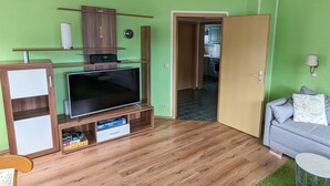 A living room with a flat-screen TV, wooden entertainment unit, and a grey sofa. - Strandnest holiday apartment (Karlshagen)