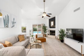 A modern living room with a sofa, coffee table, TV, fireplace, and a ceiling fan. - Perfect AZ getaway - VALVISTALIVING (Gilbert)