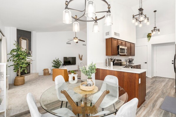 A modern living room with a glass dining table, comfortable seating, a flat-screen TV, and a fireplace. - Perfect AZ getaway - VALVISTALIVING (Gilbert)