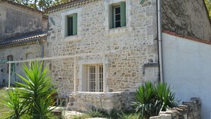 A stone building with two windows, a door, and a small garden area with plants.