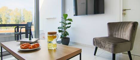 A modern living room with a wooden table, a potted plant, a television mounted on the wall, and a comfortable armchair.