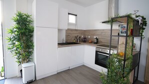 Cocina moderna con armarios blancos, encimera de madera y horno empotrado. Se observan dos macetas, un lavamanos de acero inoxidable y una ventana sobre el lavamanos.