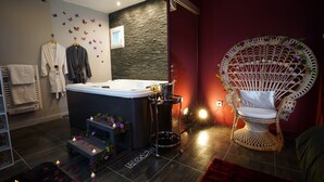 Un baño moderno con una bañera, una silla decorativa y una mesita con velas.