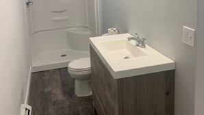 Ein Badezimmer mit Toilette, einem Holzkosmetikschrank mit Waschbecken und einer Duschkabine.