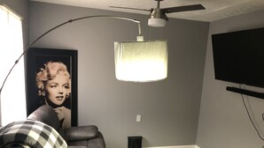 A room with a gray sofa, a black TV, a ceiling fan, and a poster on the wall. - 1220 Hartford Avenue <br> Previous 4 star owner , Airbnb<br>Happy New Year to All (Atlanta)