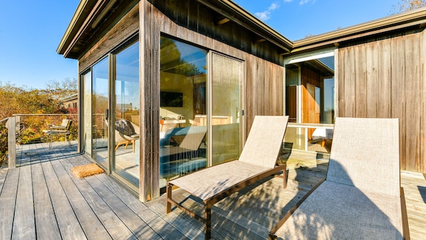 A modern deck with two lounge chairs and a glass-enclosed room.