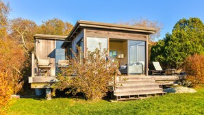 A modern wooden cabin with a deck, large windows, and a view of the surrounding trees.