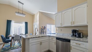 A modern kitchen with white cabinets, stainless steel appliances, and a dining area with blue chairs and a table. - New! Cozy Modern Pool Home, Close to Downtown and The Strip (North Las Vegas)