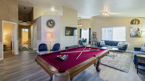 A pool table in a living room with a sofa and chairs, a TV, and a fireplace. - New! Cozy Modern Pool Home, Close to Downtown and The Strip (North Las Vegas)