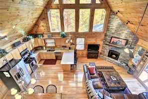 A spacious loft-style interior with a kitchen, dining area, and living room, featuring large windows and a stone fireplace.