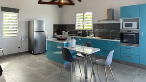 A modern kitchen with a central island, stainless steel appliances, teal cabinetry, and a wooden ceiling structure. - VILLA PAMEYAQUE T3 SUPERB SEA VIEW AND SWIMMING POOL (Rivière-Salée)