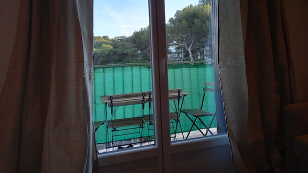 Una stanza con una grande finestra che si affaccia su uno spazio verde esterno con tavolo e sedie.