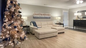 Ein Wohnzimmer mit einem beigefarbenen Ecksofa, einem Weihnachtsbaum und einem Deckenventilator.
