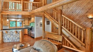 Una cabaña espaciosa con techo alto, interior de madera, chimenea de piedra y un rincón de estar acogedor.