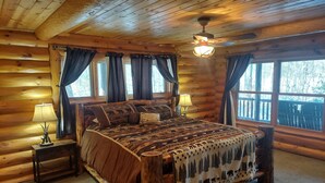 Un dormitorio de cabaña de madera con una cama, dos mesitas de noche y un ventilador de techo.