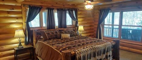 Une chambre dans une cabane en rondins, avec un lit, deux tables de chevet et un ventilateur de plafond.