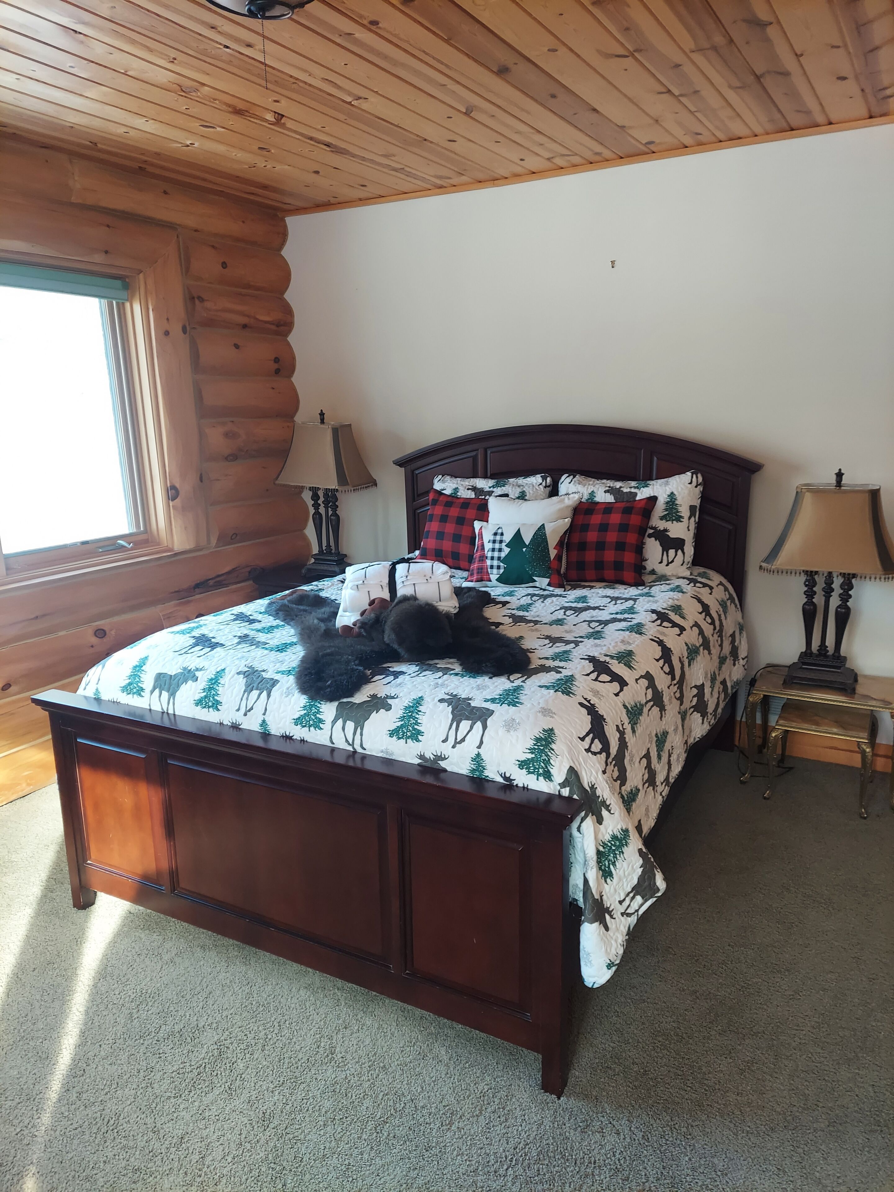 A wooden log cabin bedroom with a bed, two bedside lamps, and a window.