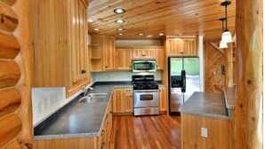 Cocina estilo cabaña de troncos con paredes y techo de madera, electrodomésticos de acero inoxidable y encimera de granito.