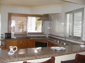 A kitchen with granite countertops, wooden cabinets, a built-in oven, a microwave, and a window with blinds. - Apartment in Carabeo near Burriana beach (Nerja)