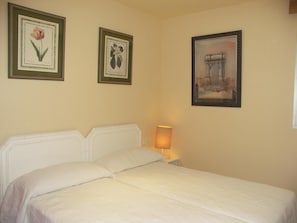 Une chambre à coucher avec un lit, une table de chevet avec une lampe et trois tableaux encadrés accrochés au mur.