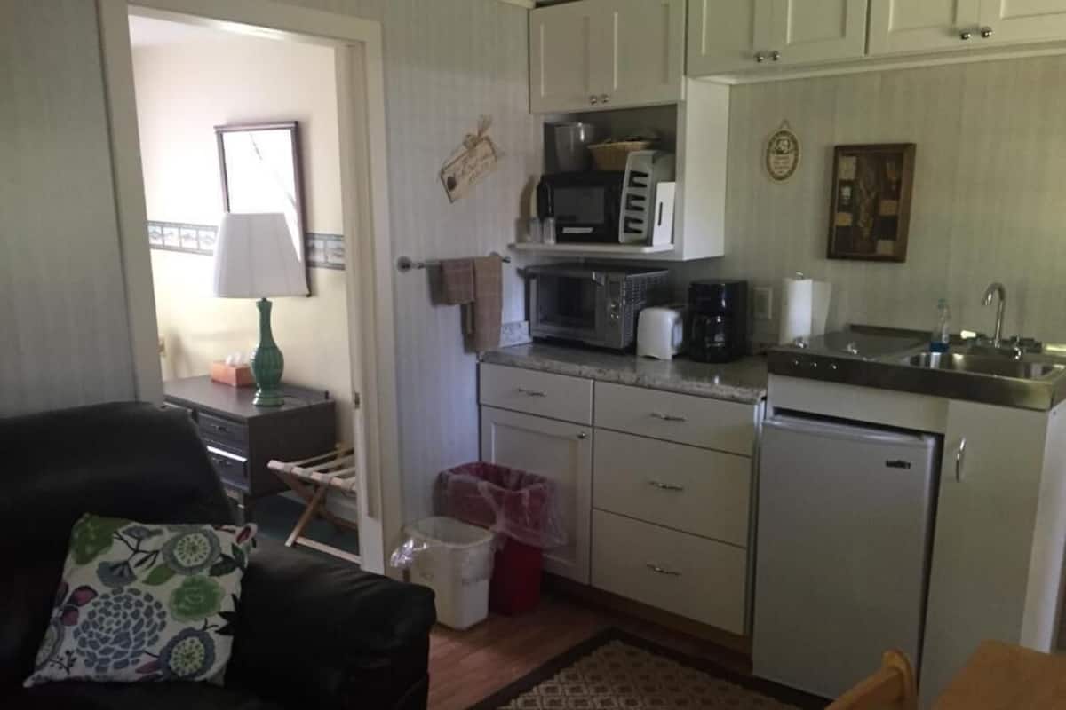Una cocina compacta con armarios blancos, un microondas, una cafetera y un refrigerador.