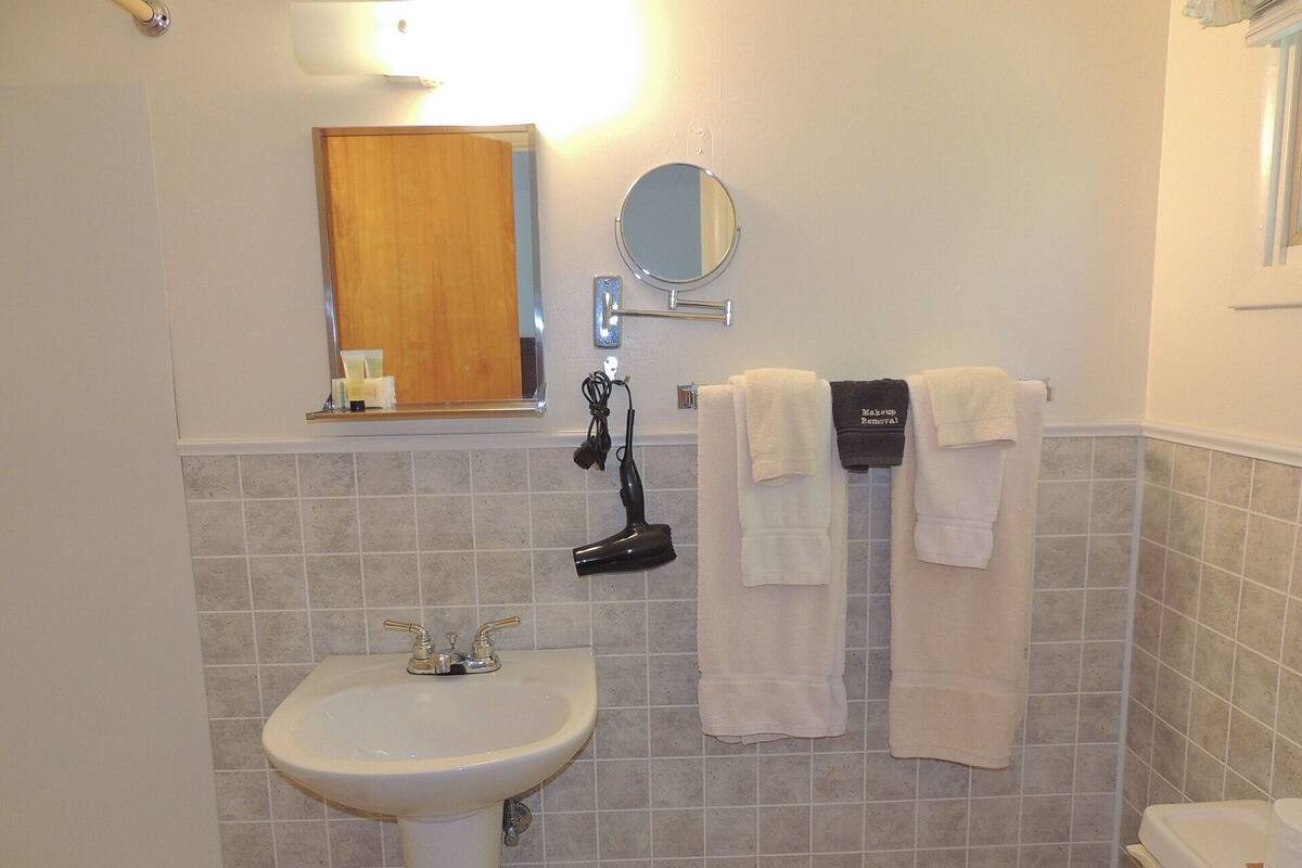 Un baño con lavamanos, espejo, toallero y secador de pelo.