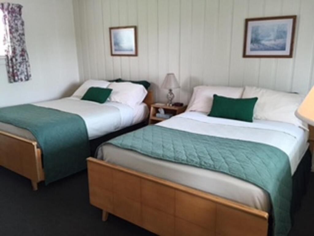 Ein Hotelzimmer mit zwei Einzelbetten, jeweils mit einem grünen Kopfkissen und einer weißen Tagesdecke. Zwei Nachttische mit Lampen stehen bereit, und die Wände sind verpanelt.