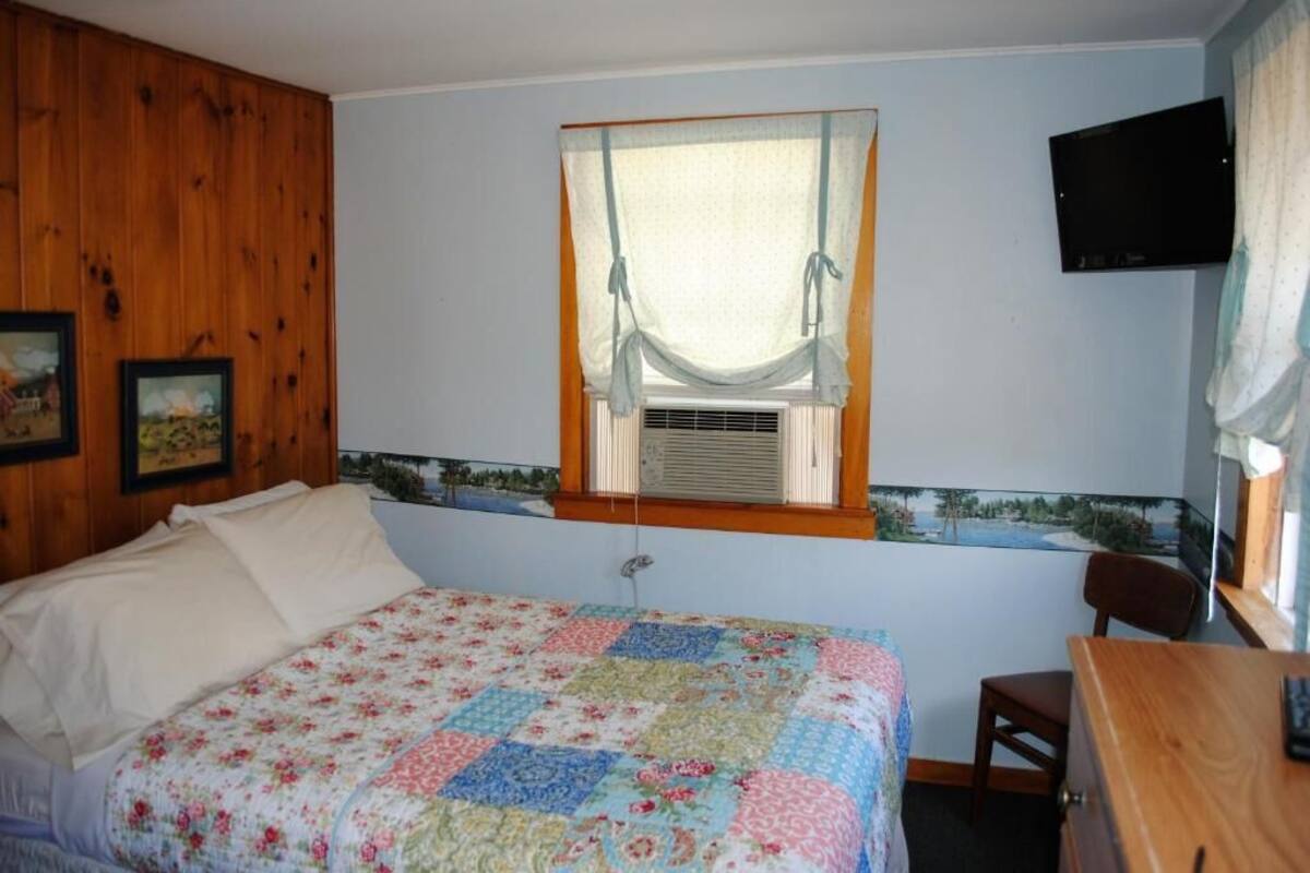 Un dormitorio con una cama, una ventana con cortina, un televisor en la pared y un cabecero de madera.