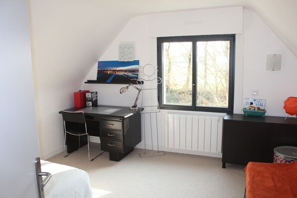 A room with a desk, chair, radiator, window, and a view of trees.