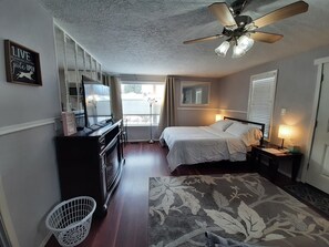 Une chambre d’hôtel comprenant un lit, une table de chevet, une lampe, un ventilateur de plafond, une commode et une vue sur l’extérieur.