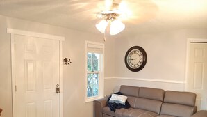 Una habitación con un sofá color beige, un reloj en la pared y una puerta con un adhesivo de un gato.