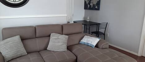 A brown sectional sofa with three pillows, a world map painting, and a clock on the wall.