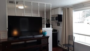 Una sala de estar con un televisor de pantalla plana sobre un soporte de madera, un pequeño jarrón azul y una silla.