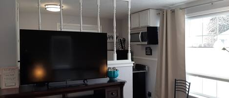 Una sala de estar con un televisor de pantalla plana sobre un soporte de madera, un pequeño florero azul y una silla.