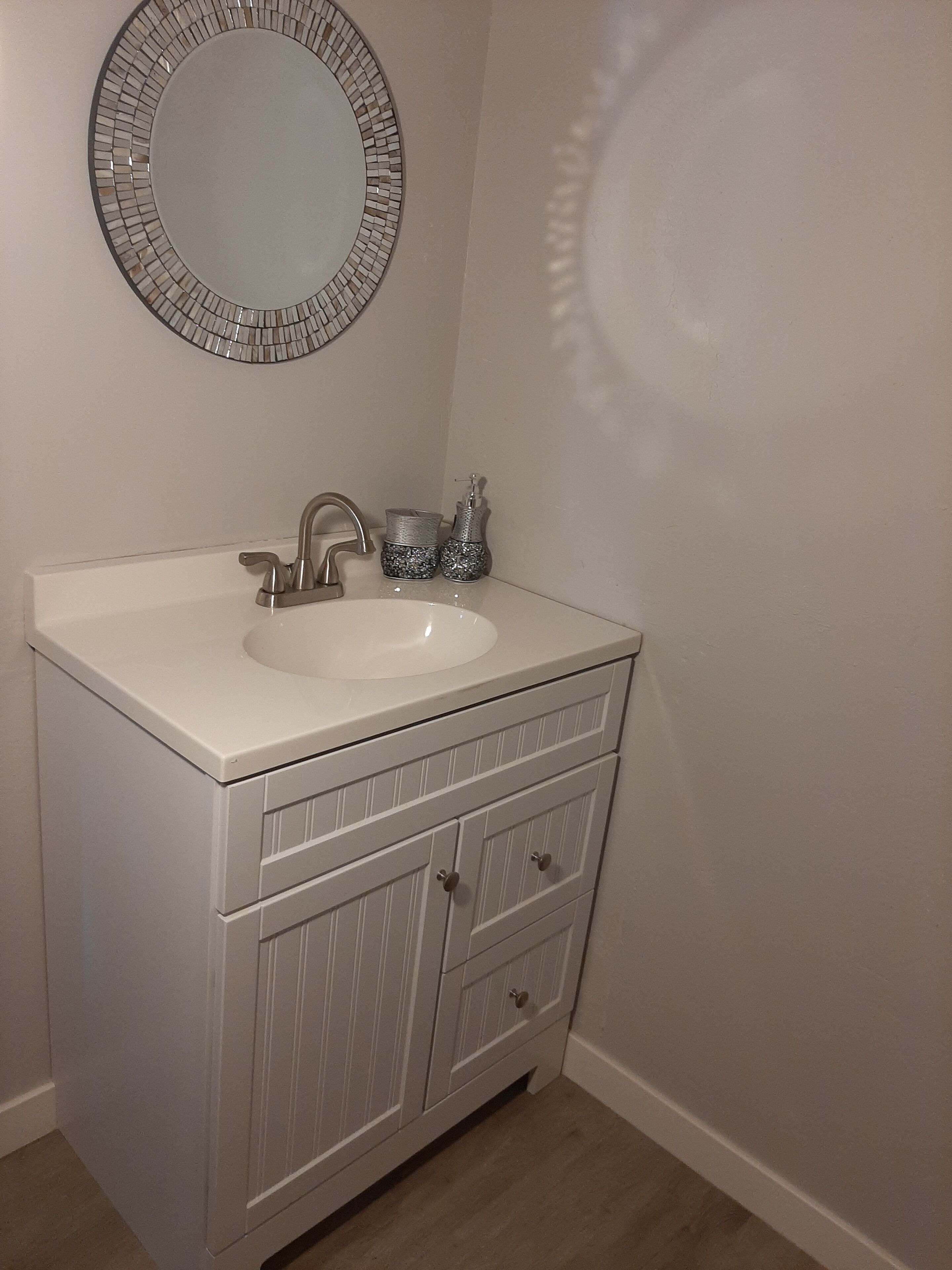 A bathroom with a white vanity, a sink, a mirror, and a faucet.