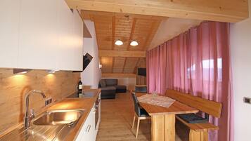 Eine moderne Küche mit Holzarbeitsplatte und Edelstahlspüle. Es gibt einen Essbereich mit Holztisch und Bank. Der Raum verfügt über Holzbalken an der Decke und rosa Vorhänge.