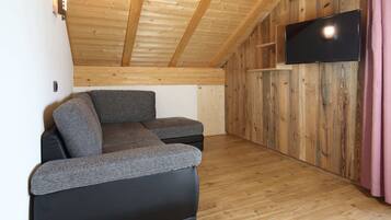 Ein moderner, kompakter Wohnraum mit Holzboden und -wänden, einem an der Wand befestigten Flachbildfernseher und einem Ecksofa.