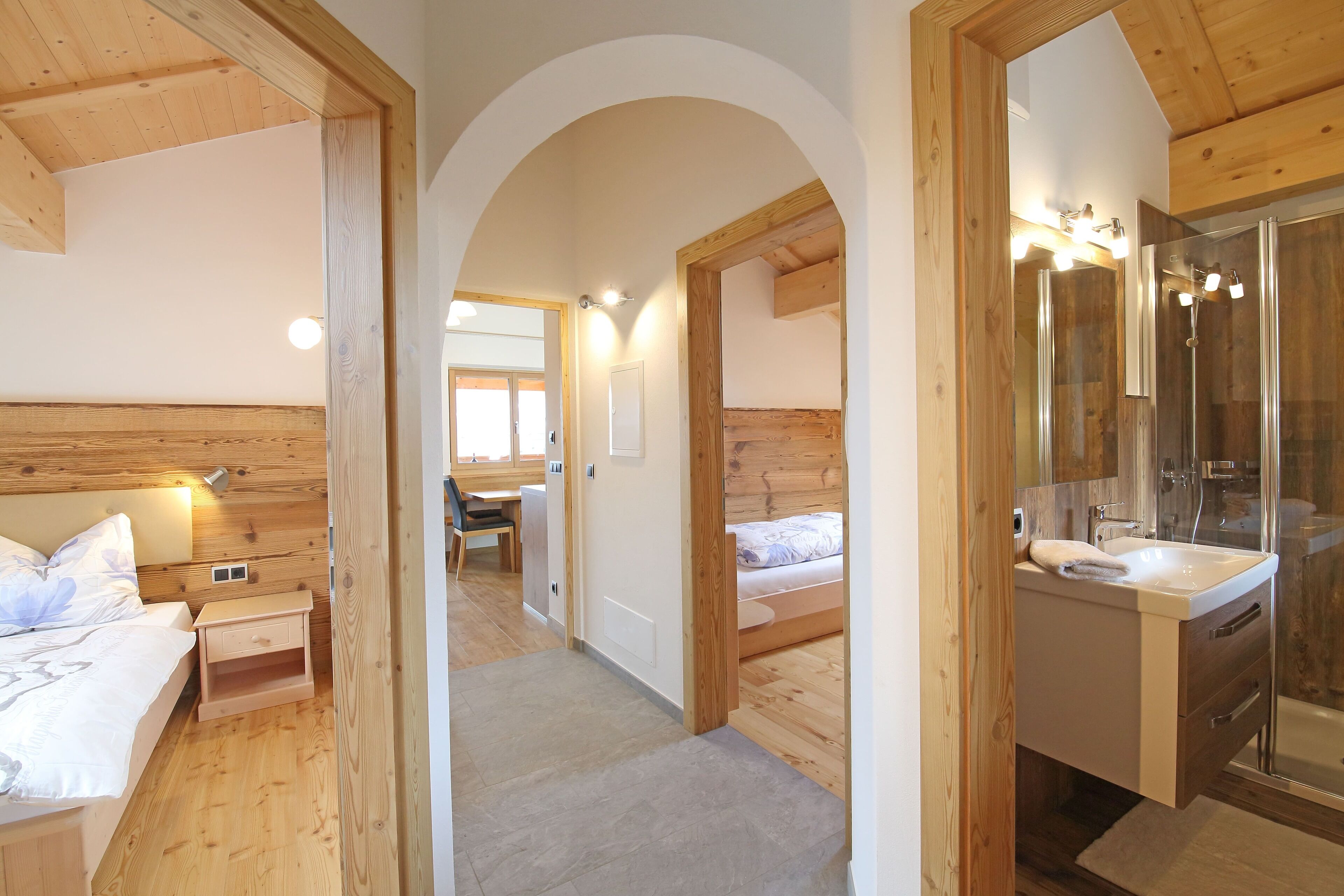 Ein Zimmer mit Holzvertäfelung, das ein Schlafzimmer, ein Badezimmer mit Glasdusche und einen Flur umfasst.