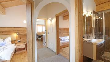 Ein Zimmer mit Holzvertäfelung, das ein Schlafzimmer, ein Badezimmer mit Glasdusche und einen Flur umfasst.