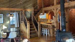 Una cabaña de madera espaciosa con techo alto, una escalera central, una chimenea grande y una zona de estar acogedora con sofá y sillones.