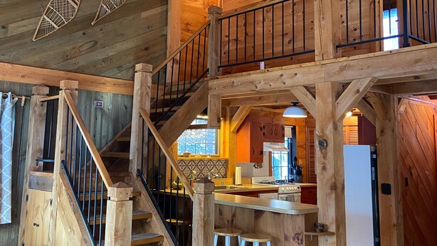 Interior de madera con una escalera que sube a un segundo piso, una zona de cocina y un comedor.