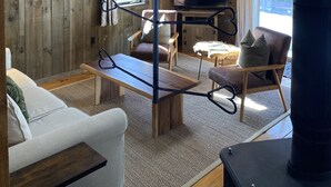 Interior acogedor de una cabaña con techo de madera, una lámpara colgante, chimenea y televisor.