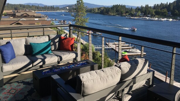 Un balcon agrémenté d’un canapé et de coussins, donnant sur une marina où sont amarrés des bateaux, et offrant une vue dégagée sur l’eau et les montagnes au loin.