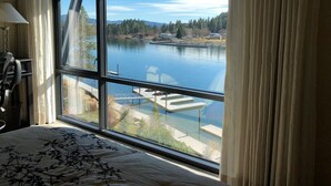Une chambre avec une grande fenêtre donnant sur un lac, un quai et la forêt environnante.