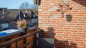 Un balcón con un muro de ladrillo, una maceta colgante, una planta en maceta y una silla de metal.